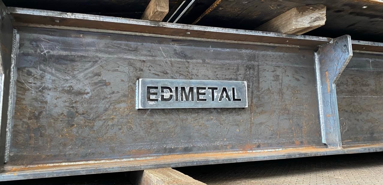 Placa de acero estampada con el nombre EDIMETAL sobre una viga metálica fabricada por la empresa